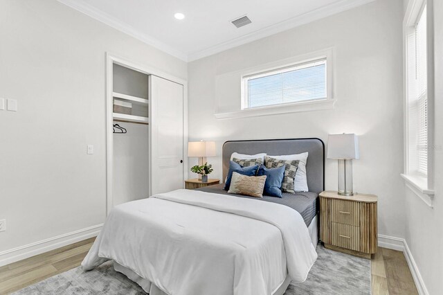 bedroom with light hardwood / wood-style floors, crown molding, and a closet