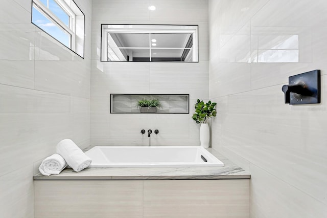 bathroom featuring a relaxing tiled tub and tile walls