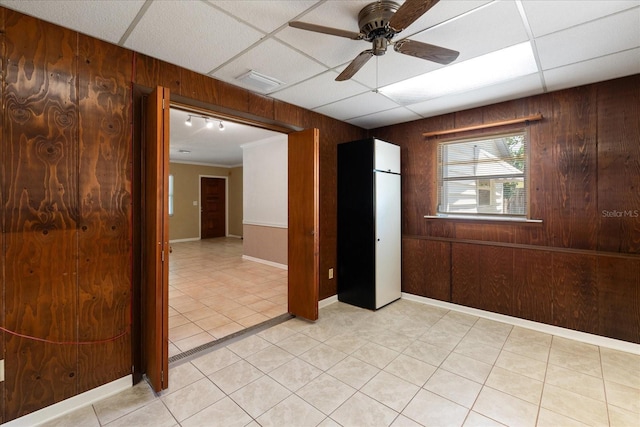 unfurnished room with light tile patterned flooring, ceiling fan, wooden walls, a drop ceiling, and baseboards