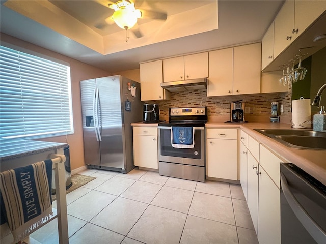 kitchen featuring a raised ceiling, light tile patterned floors, stainless steel appliances, decorative backsplash, and ceiling fan