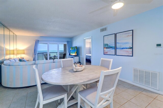 dining space featuring light tile patterned floors, ceiling fan, visible vents, and a textured ceiling