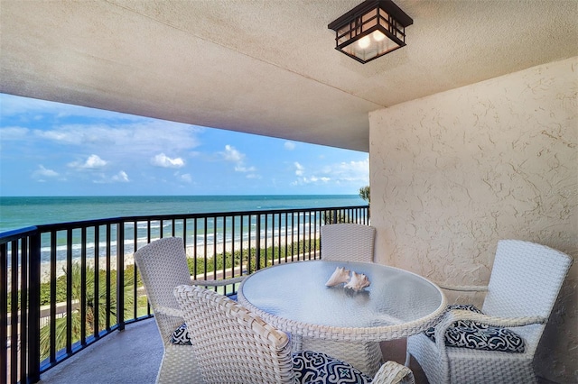 balcony with outdoor dining space, a water view, and a view of the beach