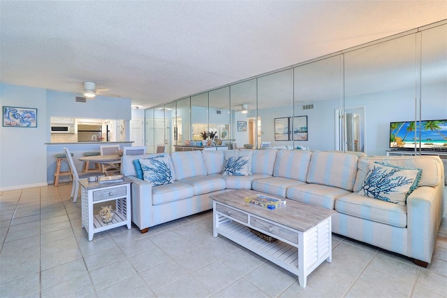 living room with light tile patterned floors, ceiling fan, visible vents, and a textured ceiling