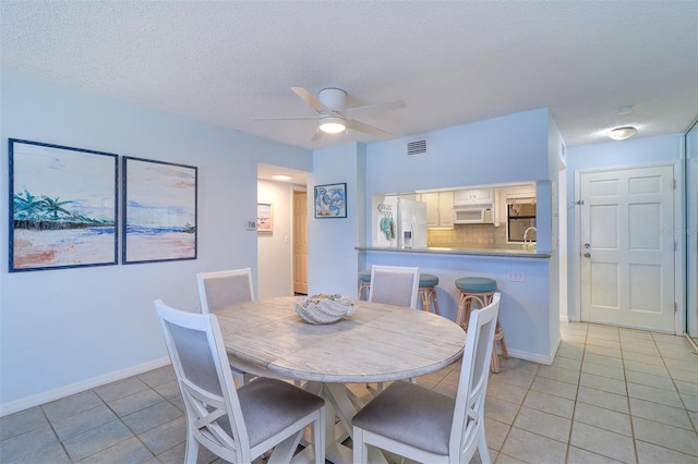 dining area featuring light tile patterned floors, visible vents, baseboards, ceiling fan, and a textured ceiling