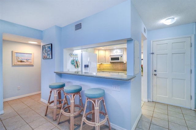 kitchen featuring a breakfast bar area, light tile patterned flooring, white appliances, visible vents, and decorative backsplash