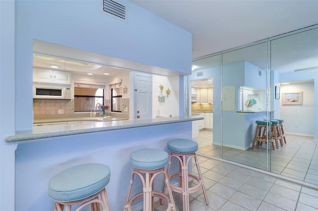 kitchen with a breakfast bar, light tile patterned floors, visible vents, decorative backsplash, and white microwave