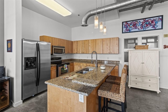 kitchen with a center island with sink, appliances with stainless steel finishes, a high ceiling, pendant lighting, and sink