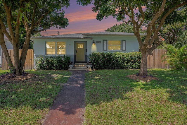 view of front of property with fence, a lawn, and stucco siding