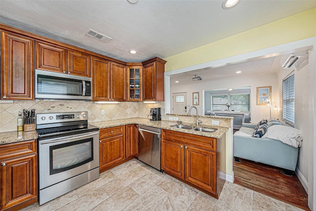 kitchen with stainless steel appliances, a sink, visible vents, open floor plan, and light stone countertops