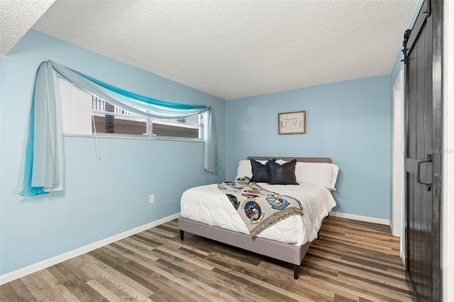 bedroom featuring a textured ceiling, a barn door, and dark wood-type flooring