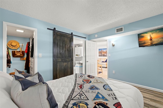 bedroom with a barn door, hardwood / wood-style floors, ensuite bath, and a textured ceiling