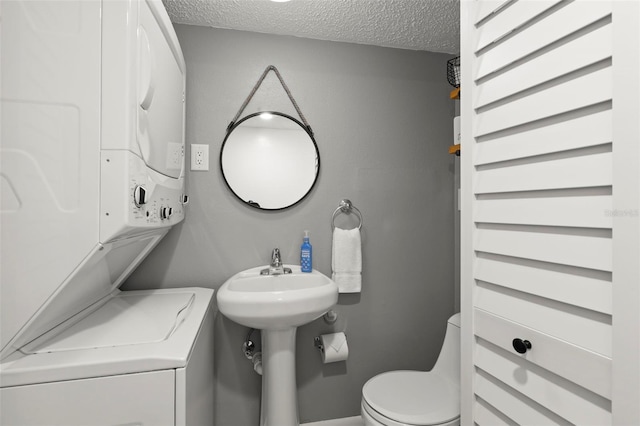 bathroom with toilet, stacked washer / drying machine, sink, and a textured ceiling