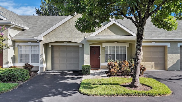 ranch-style house with a garage, aphalt driveway, roof with shingles, and stucco siding