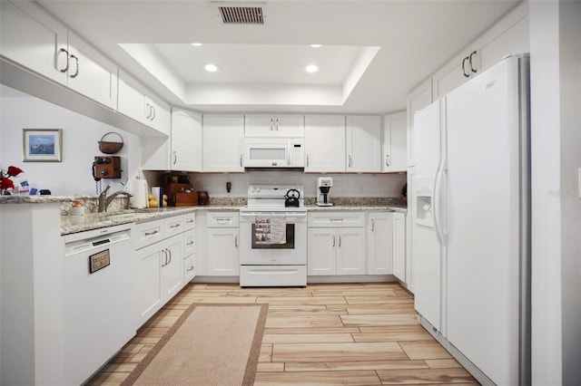 kitchen with white appliances, light stone counters, white cabinetry, a tray ceiling, and decorative backsplash