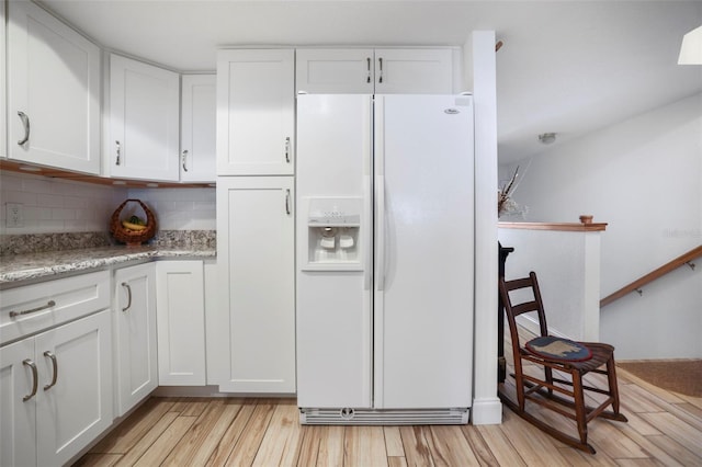 kitchen with light hardwood / wood-style flooring, backsplash, white fridge with ice dispenser, and white cabinets