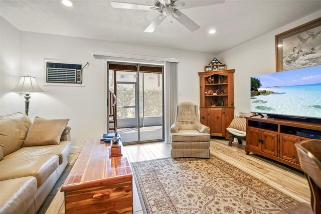 living room with a textured ceiling, a wall mounted air conditioner, light hardwood / wood-style floors, lofted ceiling, and ceiling fan