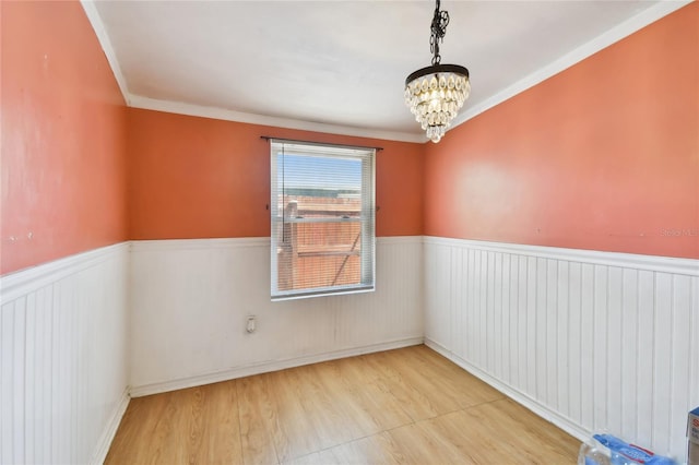 empty room featuring ornamental molding, light wood-type flooring, and a notable chandelier