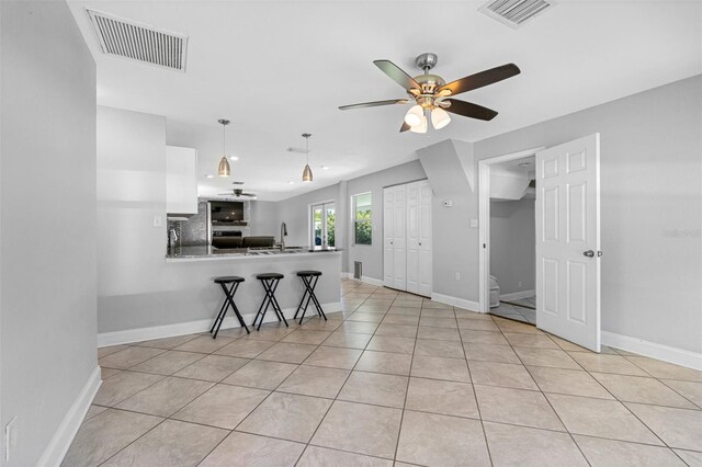 kitchen with light tile patterned flooring, a breakfast bar area, white cabinets, kitchen peninsula, and stainless steel fridge