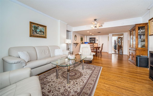 living room featuring ceiling fan, ornamental molding, light hardwood / wood-style floors, and a textured ceiling