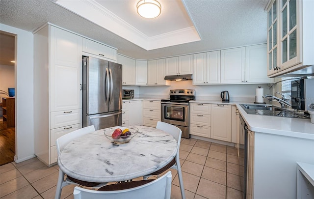 kitchen featuring ornamental molding, light tile patterned floors, stainless steel appliances, a raised ceiling, and white cabinets