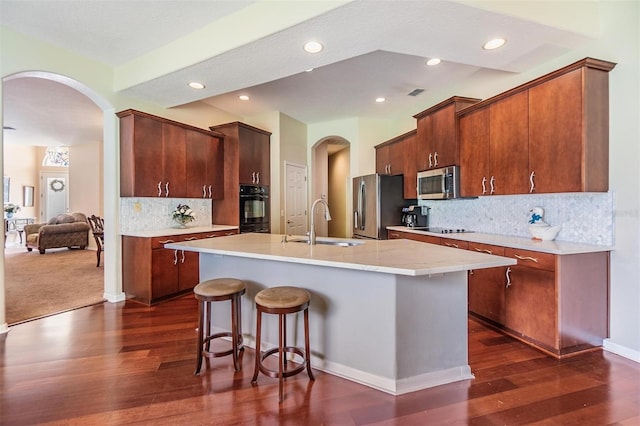 kitchen with arched walkways, light countertops, a sink, black appliances, and a kitchen breakfast bar