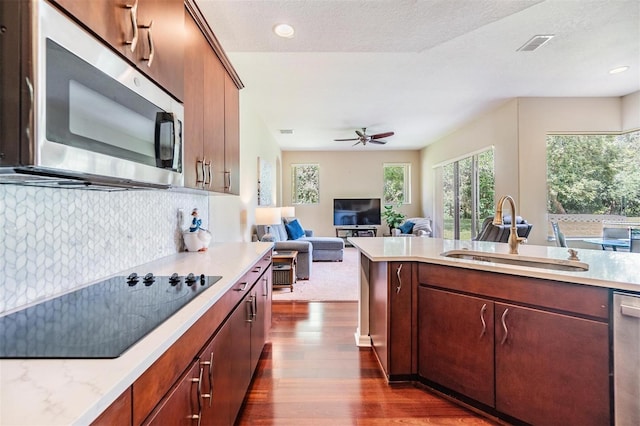 kitchen featuring decorative backsplash, dark wood finished floors, appliances with stainless steel finishes, open floor plan, and a sink