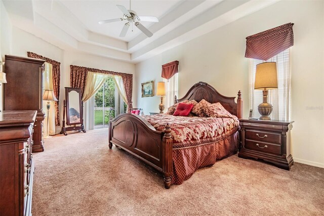 carpeted bedroom featuring ceiling fan, a tray ceiling, and access to outside