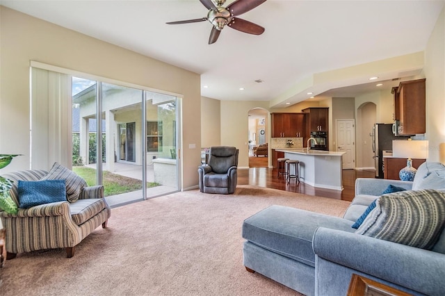 carpeted living room featuring ceiling fan, arched walkways, a sink, and recessed lighting