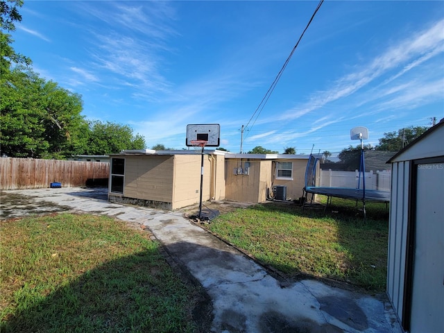 exterior space with a trampoline, a storage unit, fence, and an outbuilding