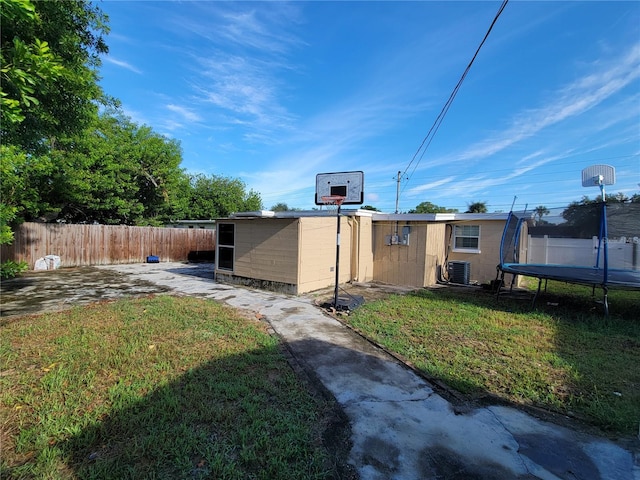 view of yard with a trampoline, fence, central AC, and an outdoor structure