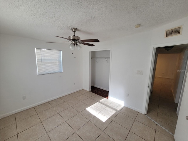 unfurnished bedroom with light tile patterned floors, visible vents, ceiling fan, a textured ceiling, and a closet