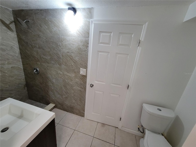 bathroom with toilet, tiled shower, vanity, and tile patterned floors