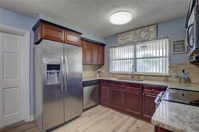 kitchen with sink, a textured ceiling, decorative backsplash, appliances with stainless steel finishes, and light wood-type flooring