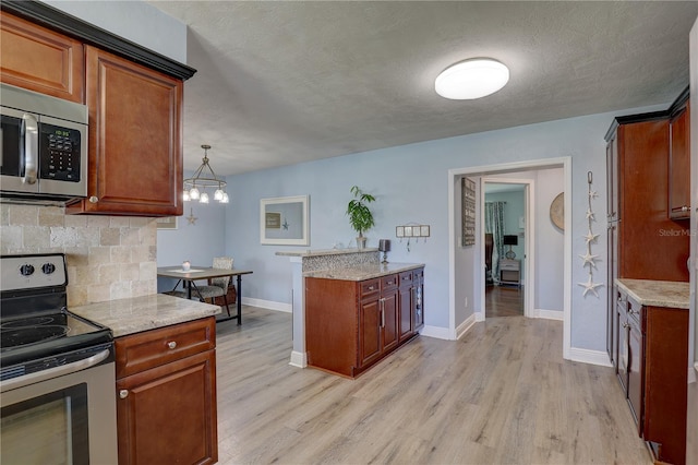 kitchen with light stone counters, stainless steel appliances, pendant lighting, a chandelier, and light hardwood / wood-style floors