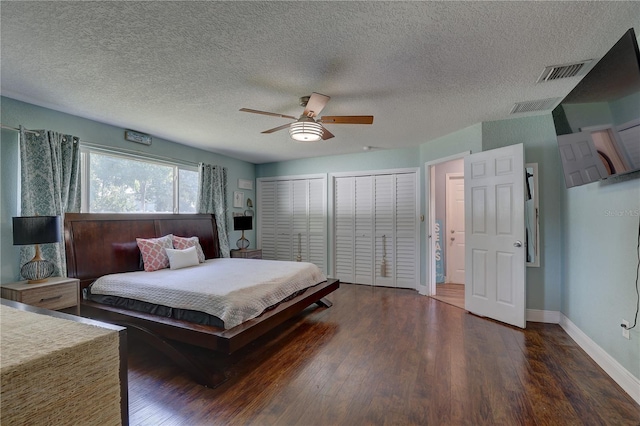 bedroom featuring ceiling fan, dark hardwood / wood-style floors, a textured ceiling, and two closets