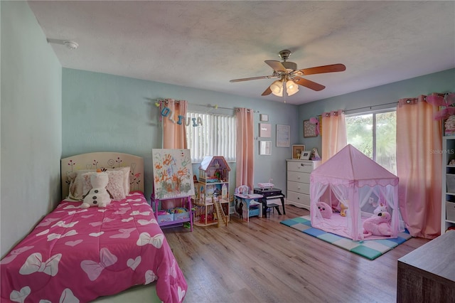 bedroom with multiple windows, wood-type flooring, a textured ceiling, and ceiling fan