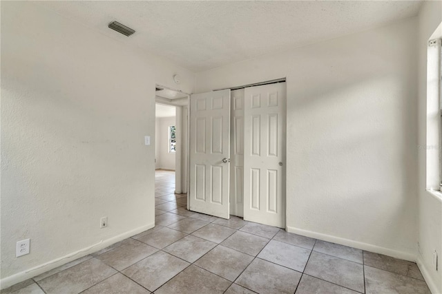 unfurnished bedroom with a textured ceiling, a closet, and light tile patterned floors