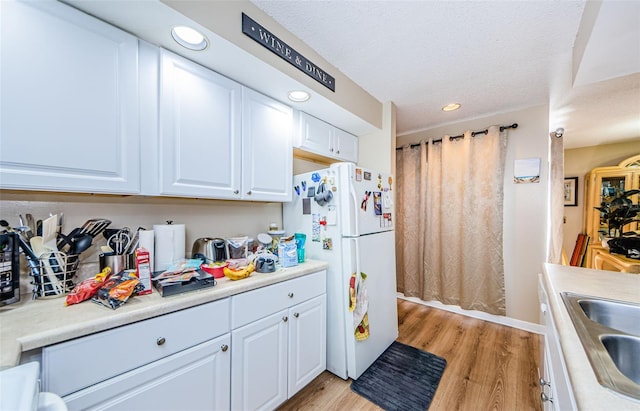 kitchen featuring white cabinetry, sink, light wood-type flooring, a textured ceiling, and white refrigerator