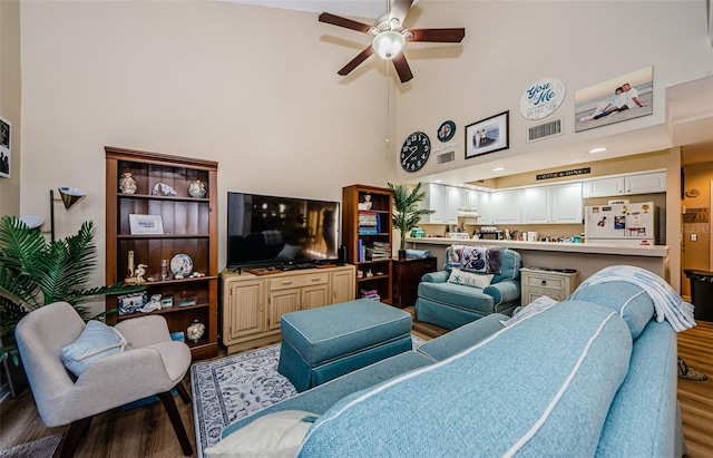 living room with ceiling fan, hardwood / wood-style floors, and a towering ceiling