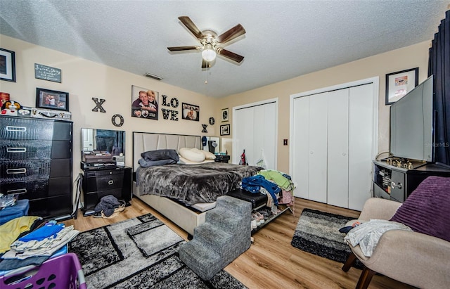 bedroom with multiple closets, light wood-style floors, a textured ceiling, and a ceiling fan