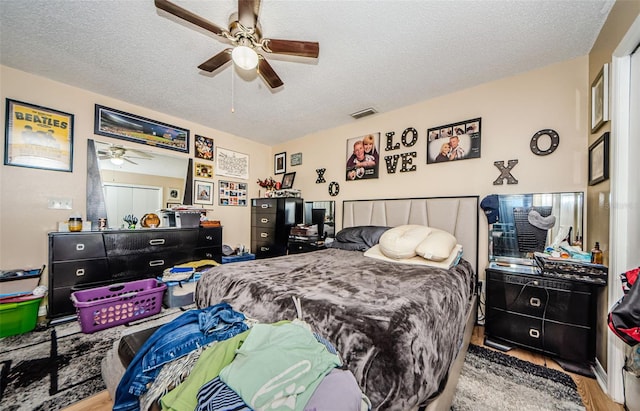 bedroom featuring ceiling fan, a textured ceiling, visible vents, and wood finished floors