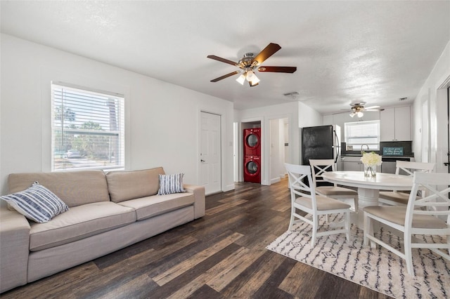 living room with ceiling fan, stacked washer / dryer, and dark hardwood / wood-style flooring