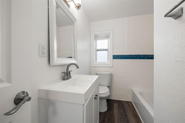 bathroom with hardwood / wood-style floors, a bath, vanity, tile walls, and toilet