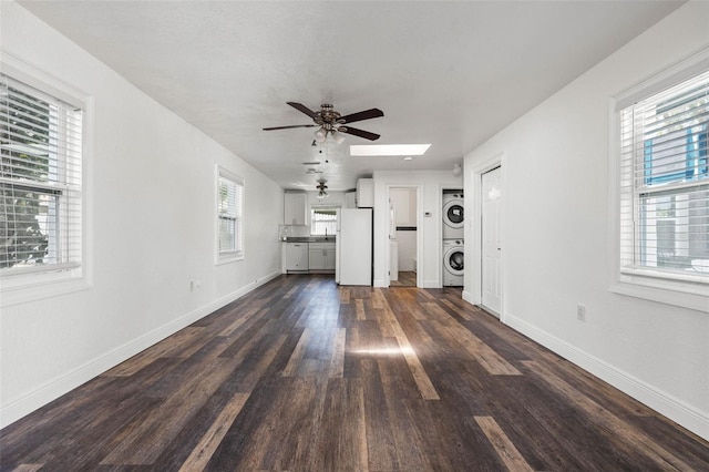 unfurnished living room featuring ceiling fan, stacked washing maching and dryer, dark hardwood / wood-style floors, and a wealth of natural light