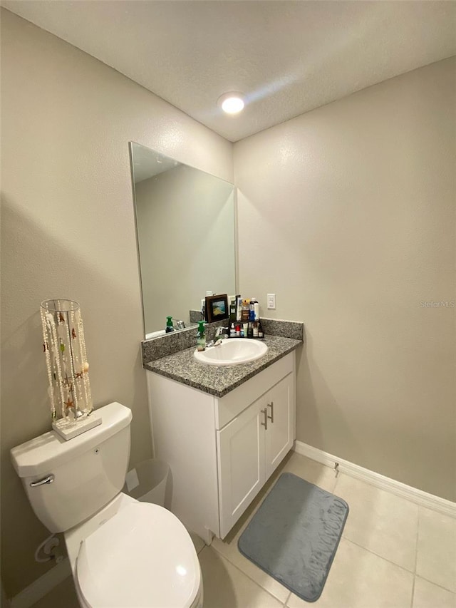 half bathroom with baseboards, vanity, toilet, and tile patterned floors