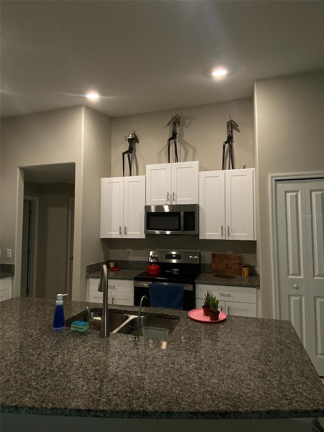 kitchen featuring stainless steel appliances, white cabinetry, a sink, an island with sink, and dark stone countertops