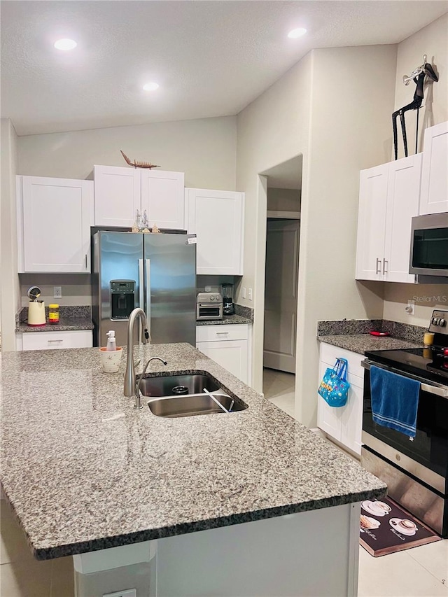 kitchen featuring dark stone counters, appliances with stainless steel finishes, a sink, and white cabinets