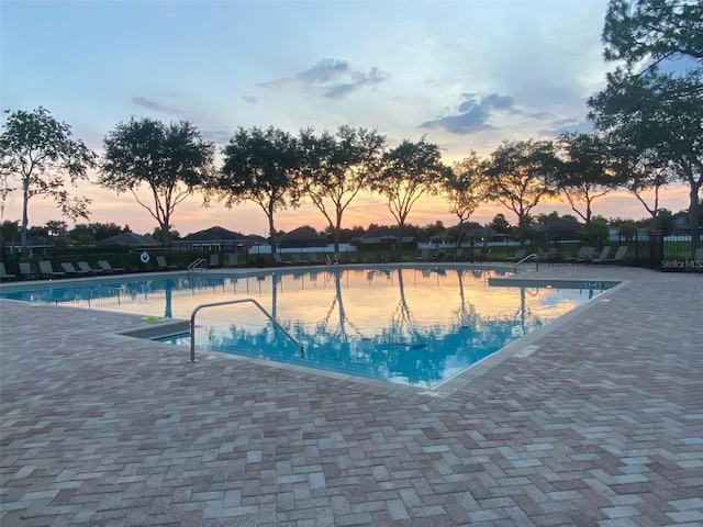 pool at dusk featuring fence, a community pool, and a patio