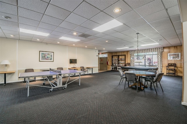 recreation room featuring wood walls, dark colored carpet, and a drop ceiling