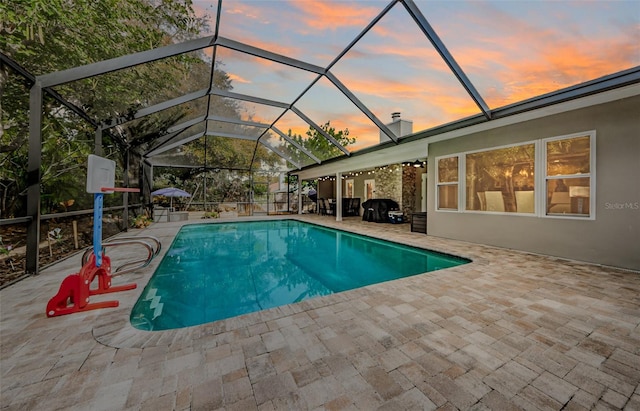 pool at dusk with a patio area and glass enclosure